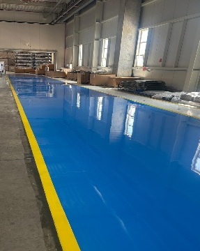 Frisch beschichtete blaue Epoxidharzfläche mit gelber Randmarkierung in einer Halle