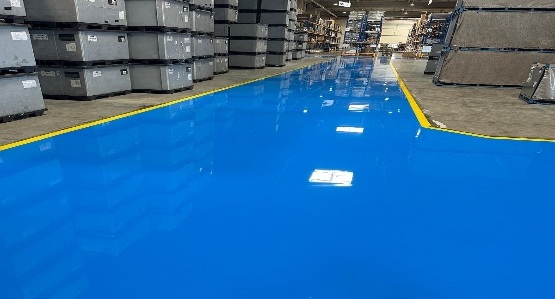 Blaue Epoxidharzfläche mit gelber Randmarkierung zwischen Gitterboxen im Lager